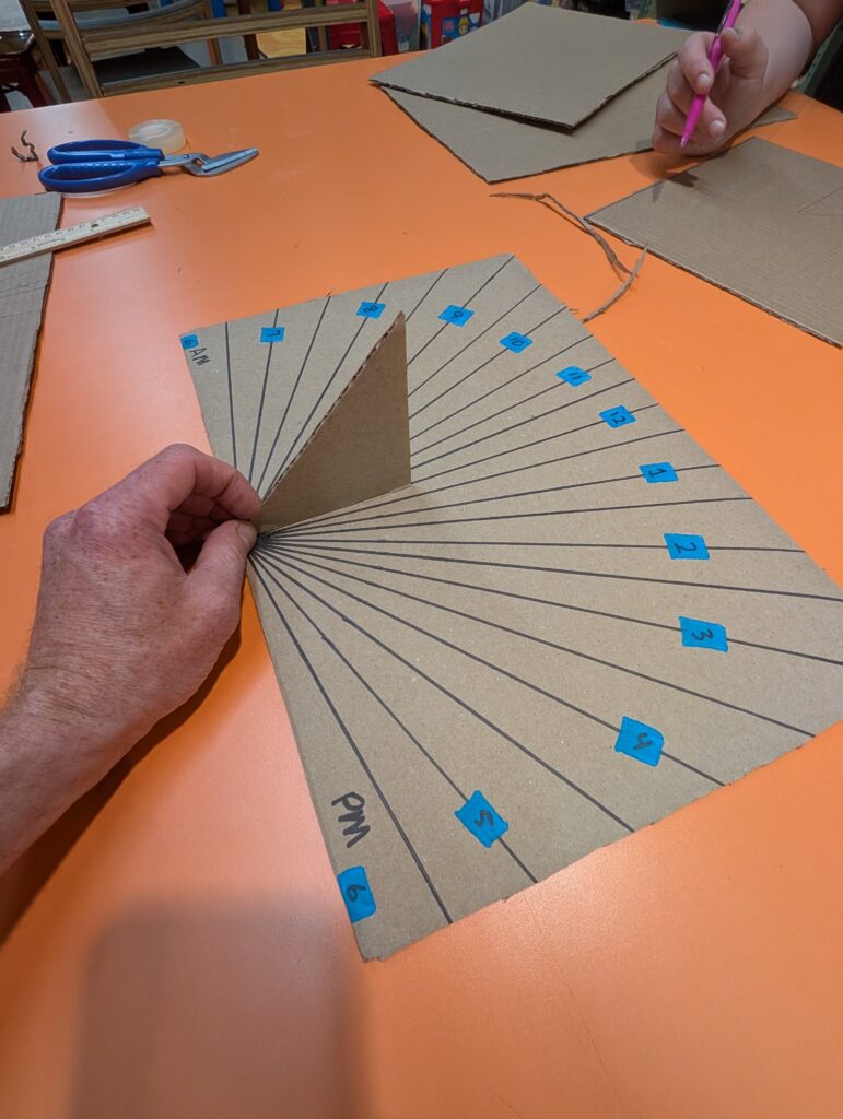 A cardboard sundial in progress, with marked hour lines and an upright shadow-casting piece.